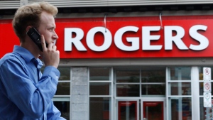 man with cellphone at his ear in front of a sing that says "Rogers"